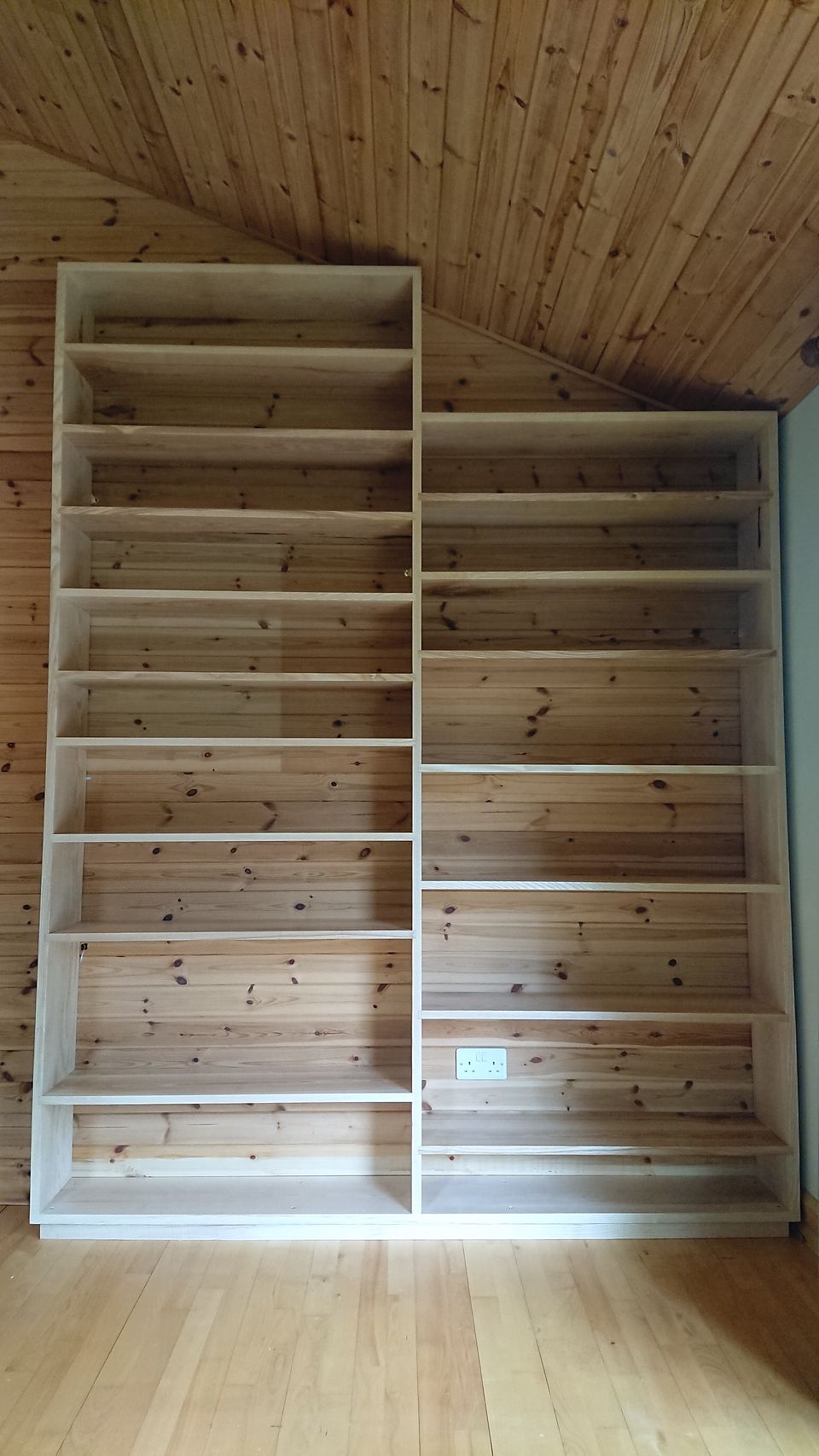 Fitted solid-wood shelving built under a sloping pine-clad ceiling