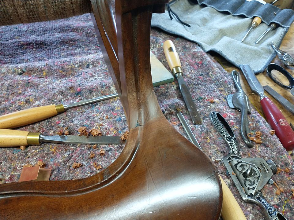 Carving chisels and tools laid out beside a cabriole leg under repair