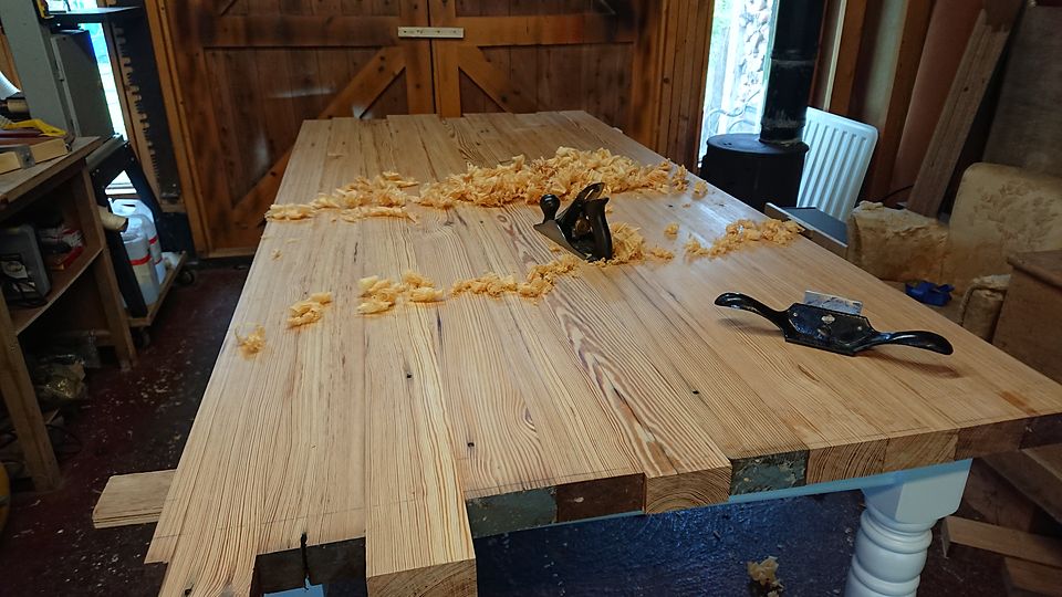 Hand planing a plank table top: plane, spokeshave and curled shavings on the boards